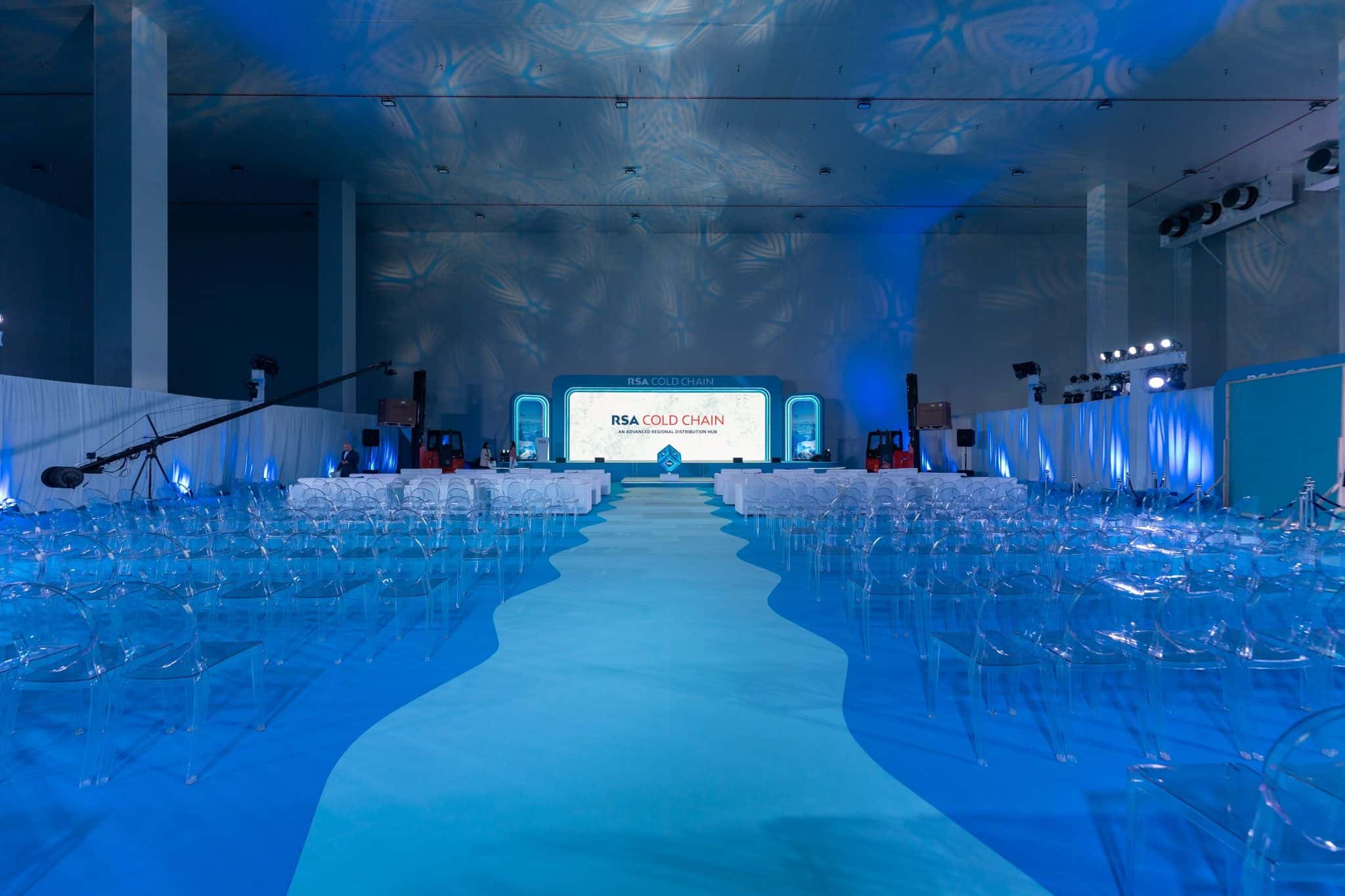 Launch hall before doors open: blue gobo light across the ceiling, a river-shaped aisle and the stage screen